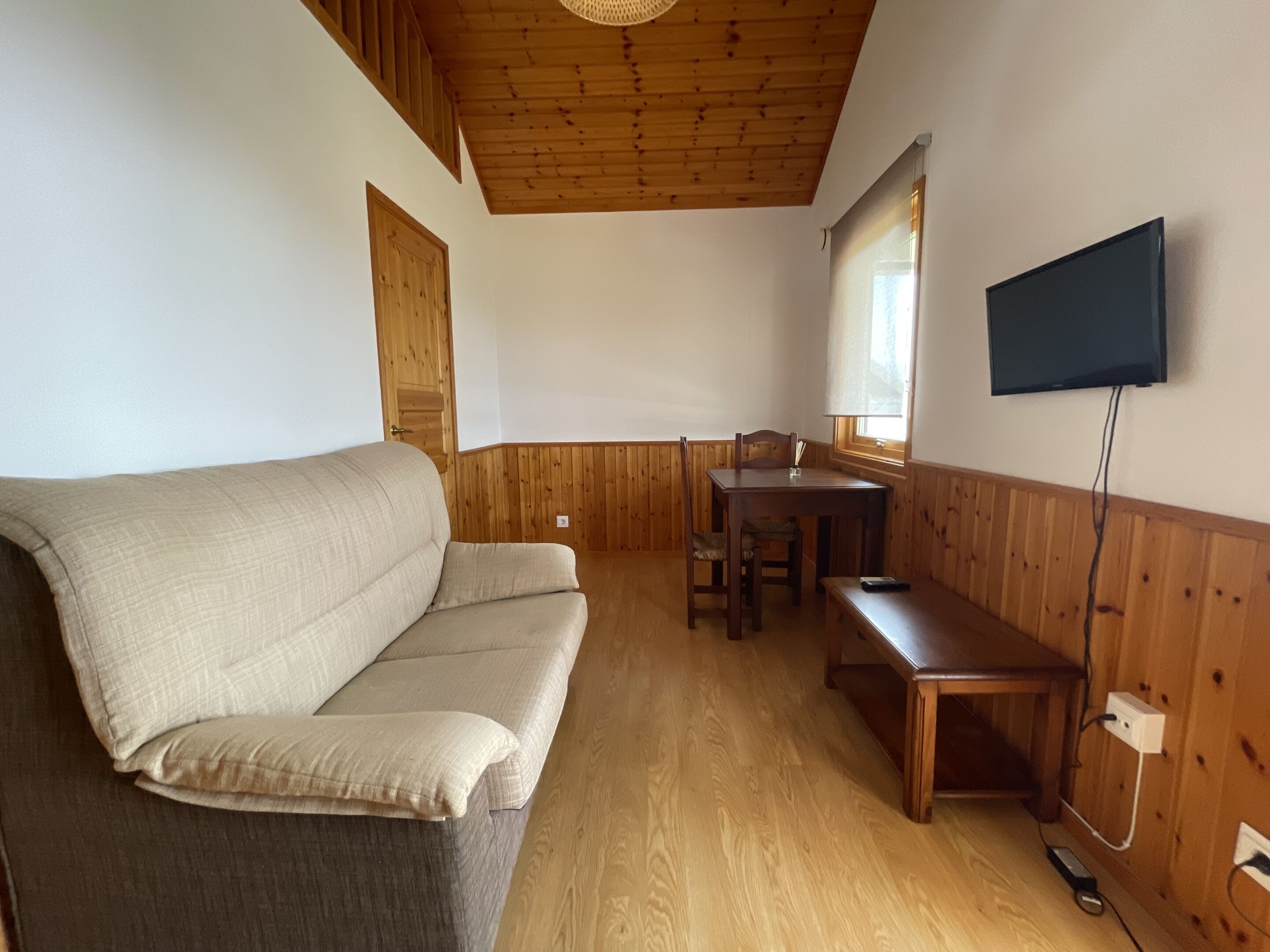 Een kamer met een bank, een houten eettafel en een aan de muur bevestigde televisie.