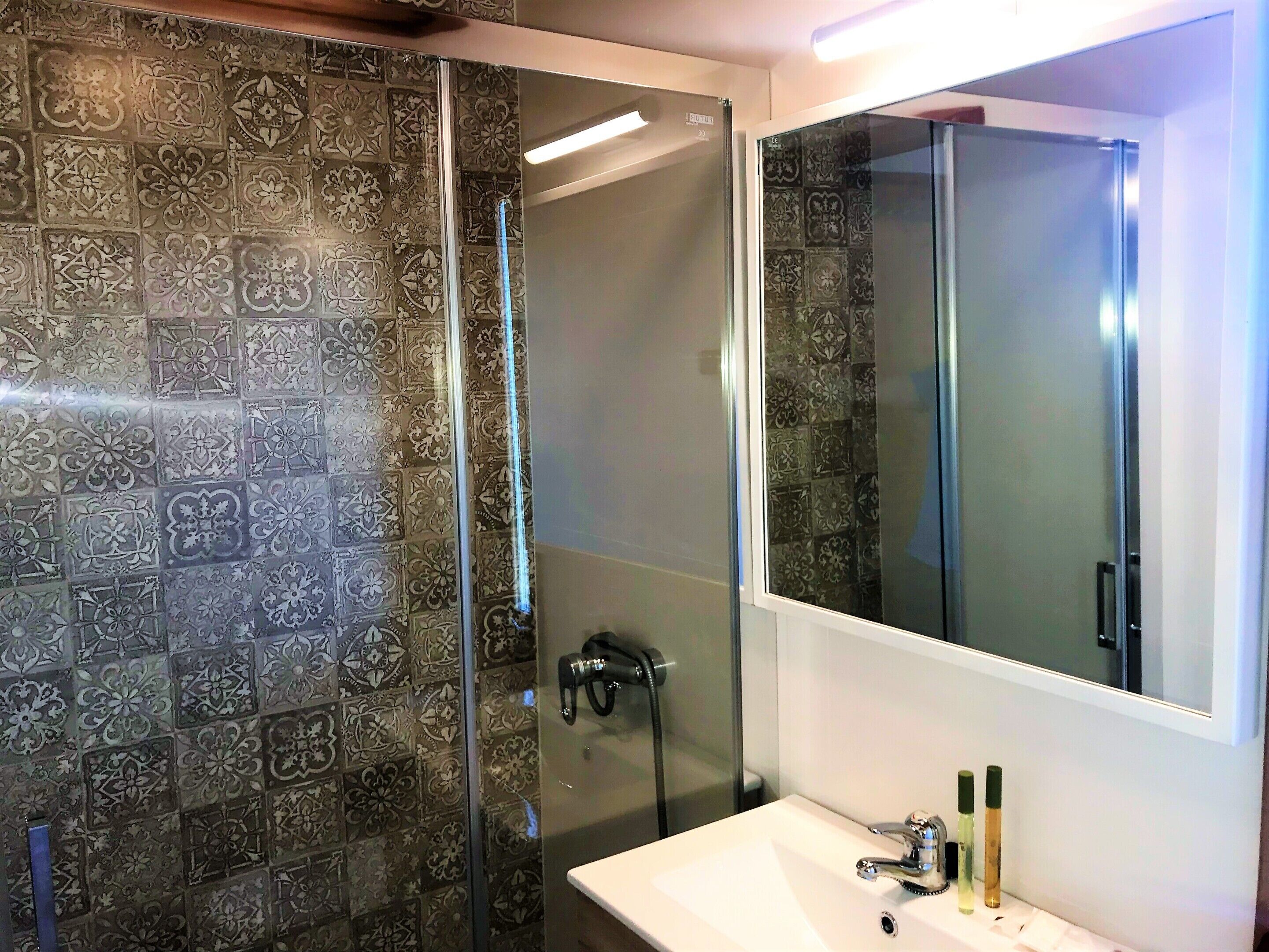 A bathroom with a glass shower enclosure, a white sink, and a large mirror.