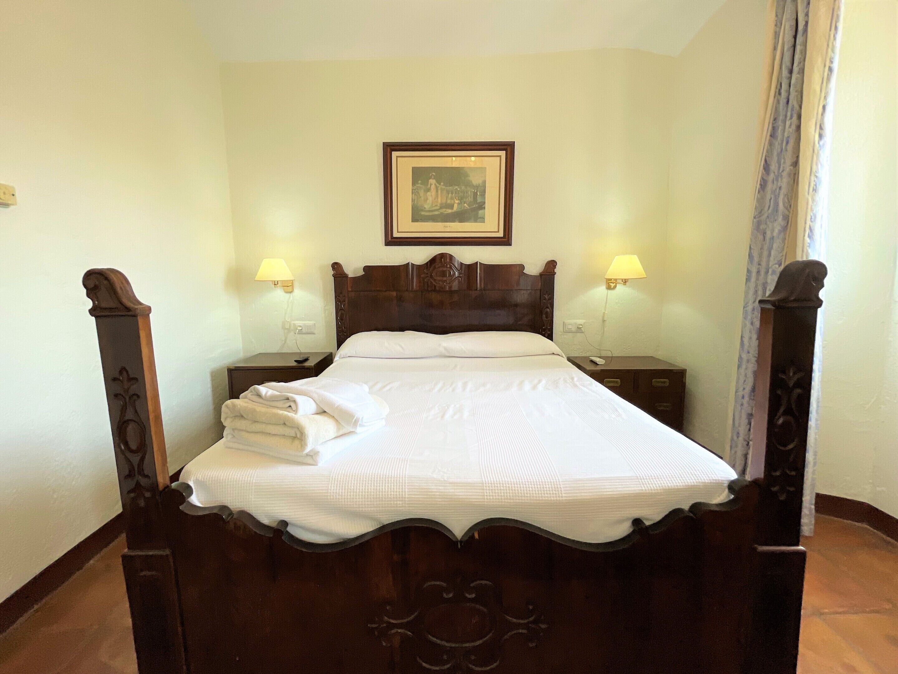 A neatly made bed with a wooden headboard, two bedside tables with lamps, and a framed picture above the bed.