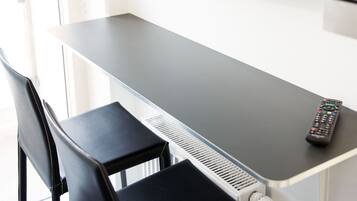 A room with a TV mounted on the wall, a desk, a chair, and a remote control on the desk.