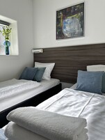Habitación de hotel con dos camas, una ventana con planta, un cuadro en la pared y un aire acondicionado de pared.