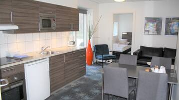 Una cocina moderna con microondas, lavaplatos y fregadero, un comedor con mesa y sillas, y una sala de estar con sofá y mesa de centro.