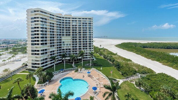 Un hotel moderno con piscina grande, playa y abundante vegetación.