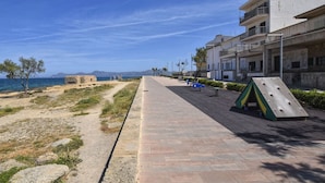 A coastal walkway with a playground, a path leading to the sea, and buildings in the background. - Harborfront Escape in Mallorca (Ca'n Picafort)
