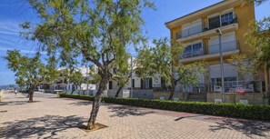 A building with a two-story structure, a balcony on the upper floor, and a paved area with trees and shrubs.