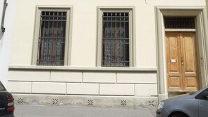 Un immeuble à plusieurs étages, doté d’une façade beige, de six fenêtres avec volets et d’une porte en bois.
