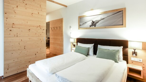 Un lit double avec une literie blanche, une tête de lit en bois et deux tables de chevet avec des lampes.