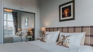 Une chambre d’hôtel avec un grand lit, un miroir, un tableau encadré au mur et une fenêtre avec des rideaux.