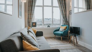 Un salon moderne avec un canapé gris, un fauteuil turquoise et un téléviseur posé sur un meuble.