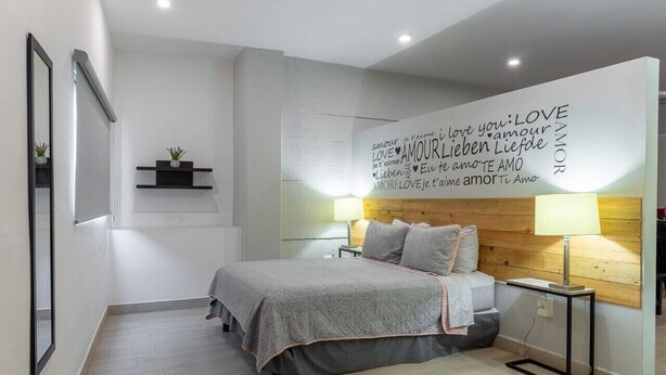 A modern bedroom with a bed, bedside lamps, a wall with love-themed text, and a small shelf with a plant. - New historic center apartment (1) 200 meters from the boardwalk  (Zona Comercial)
