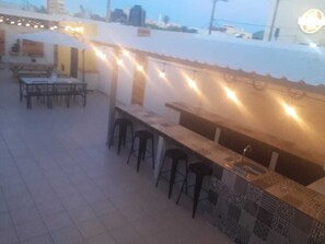 An outdoor bar area with a tiled counter, bar stools, and string lights.
