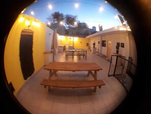 An outdoor patio area with a wooden table and benches, surrounded by yellow walls and a white fence.