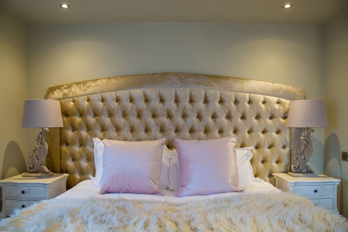 A bedroom with a tufted headboard, two bedside lamps, a fluffy white bedspread, and two nightstands.
