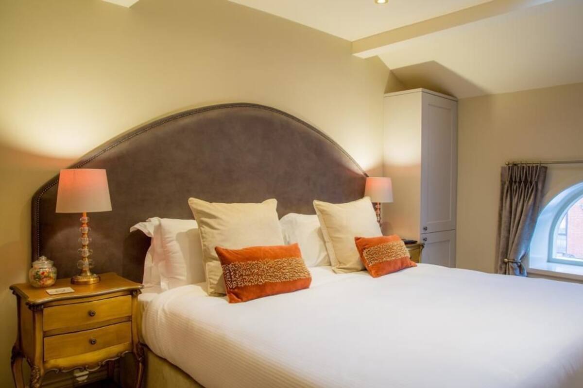 A hotel room with a large bed, two bedside tables, a nightstand, a lamp, and a window with curtains.