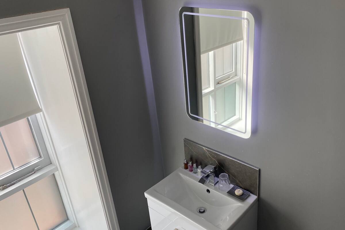 A bathroom with a white sink, a mirror, and a window.