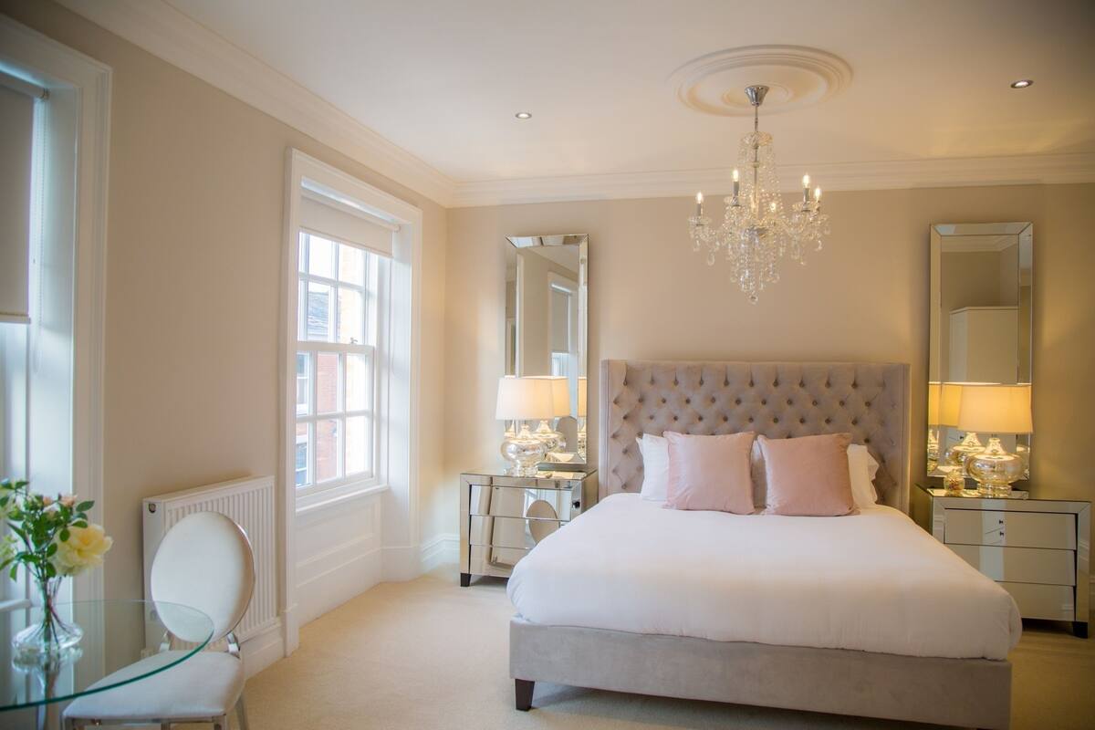A spacious bedroom with a large bed, a chandelier, and two bedside tables with lamps.