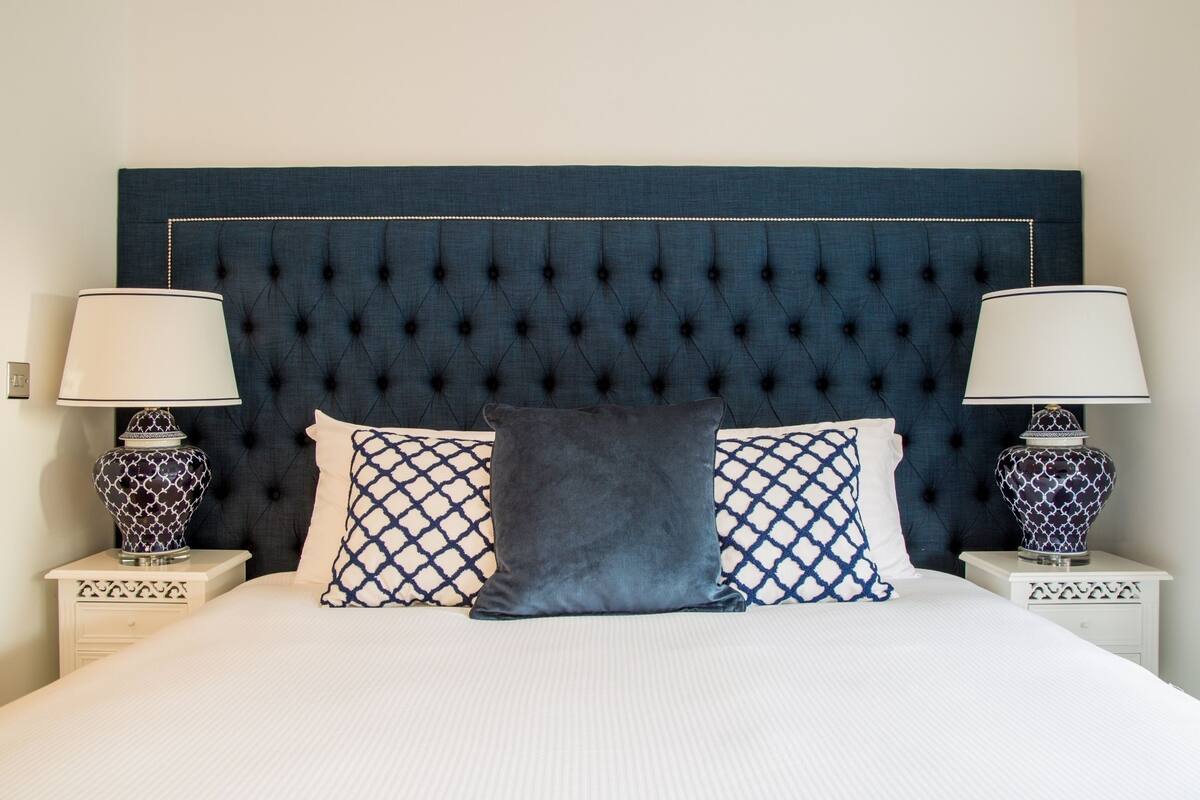 A neatly made bed with a tufted headboard, two patterned pillows, and two bedside lamps with patterned bases.