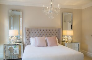 Quarto com cabeceira estofada, duas mesas de cabeceira com abajures e um candelabro.