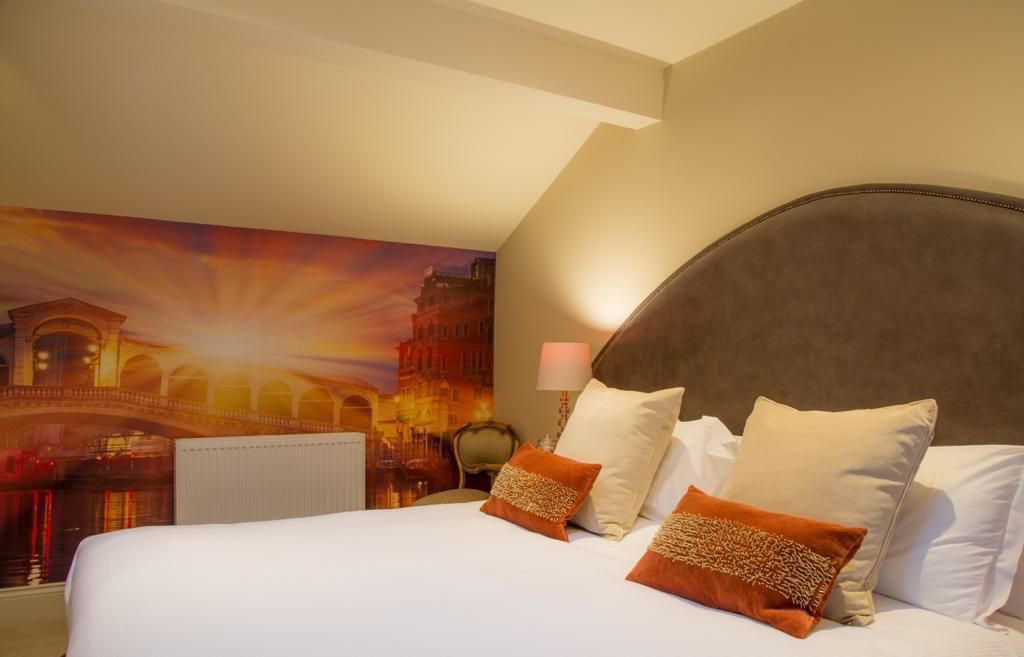 A hotel room with a large bed, a headboard, and a wall mural of a cityscape.