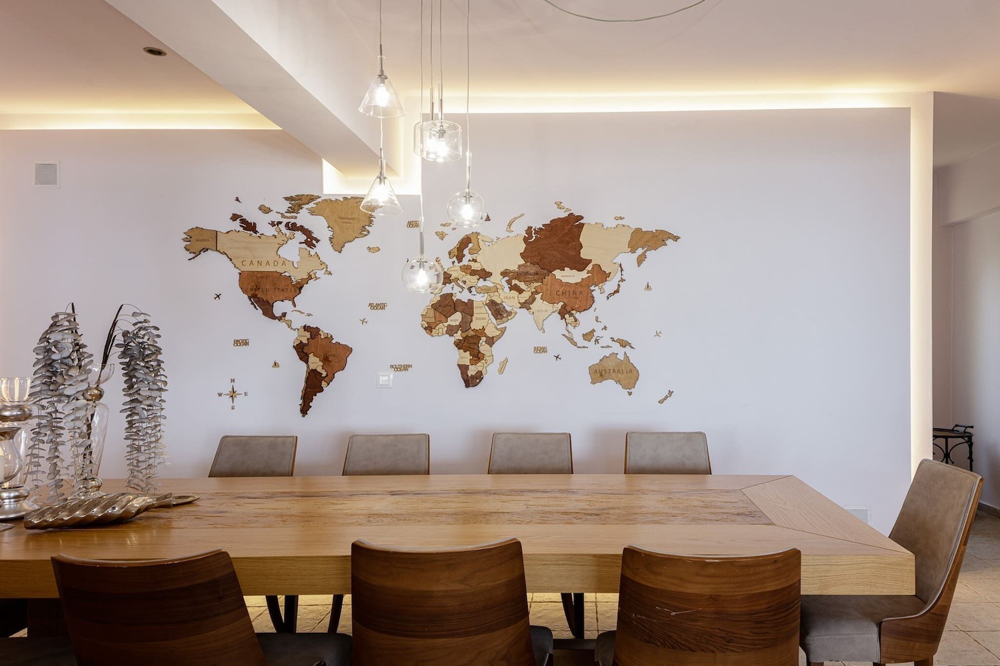 Un espace repas moderne avec une grande table en bois, six chaises et une carte du monde accrochée au mur.