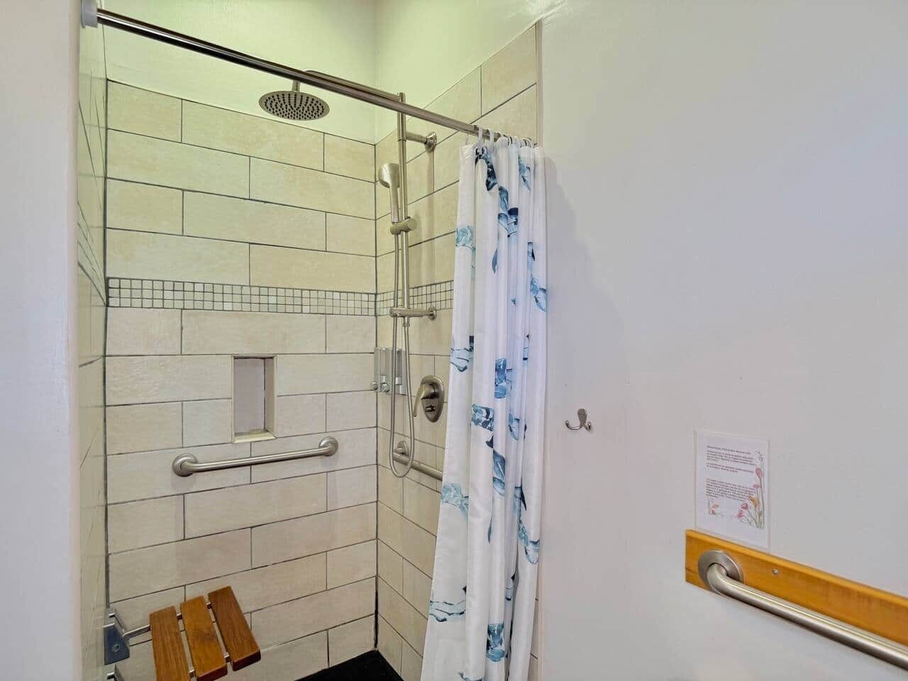 Un espace douche doté d’une porte en verre, d’une barre d’appui et d’un pommeau de douche.