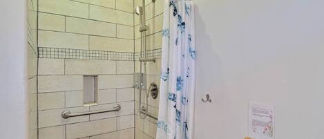 Un espace douche doté d’une porte en verre, d’une barre d’appui et d’un pommeau de douche.