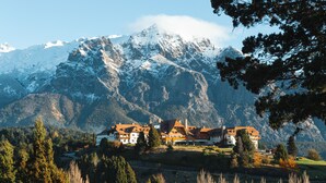 Una casa de montaña con varias construcciones, rodeada de árboles y montañas nevadas.