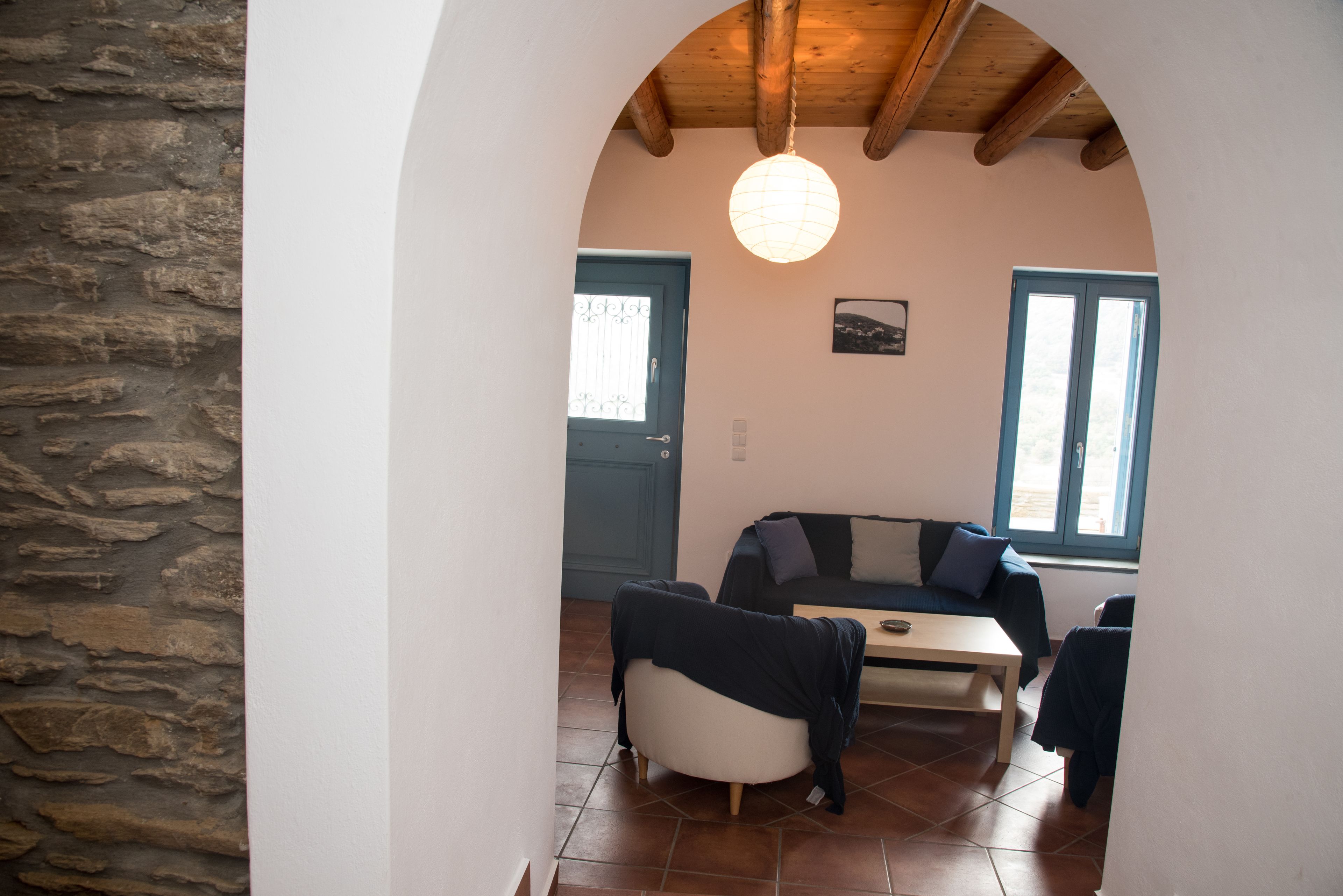 Un espacio de estar acogedor con pared de piedra, techo de madera, un sofá, una mesa y una ventana.