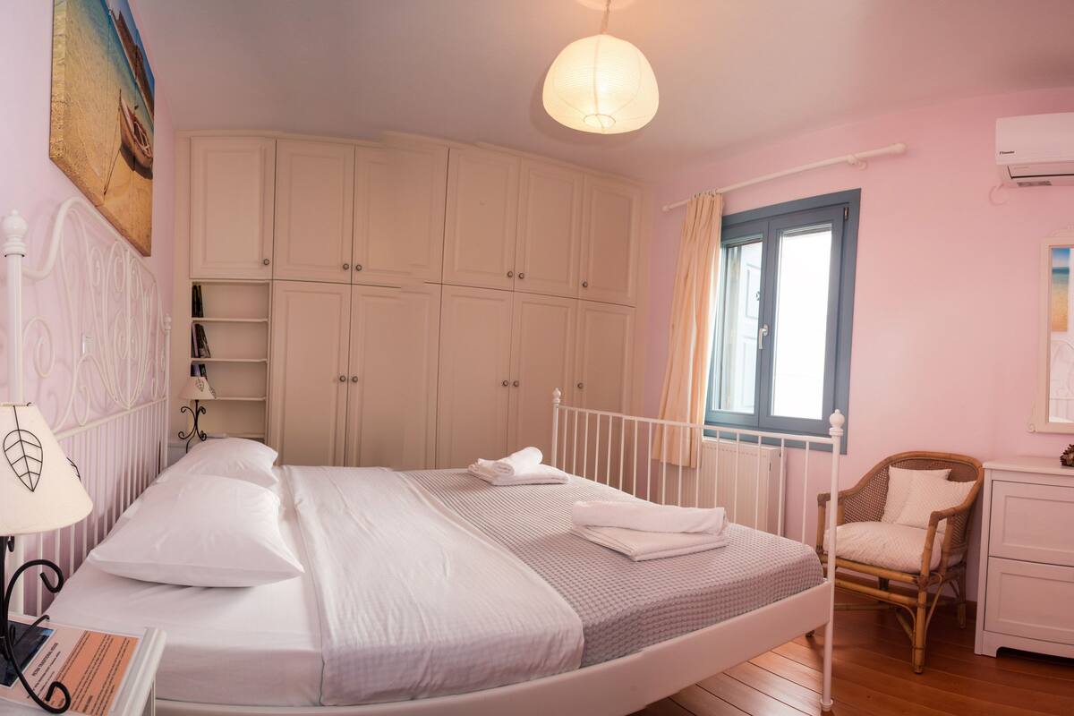 A bedroom with a bed, a nightstand, a chair, a wardrobe, and a window.