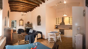 A cozy living room with a fireplace, a dining area, and a kitchen with white cabinets. - Petra Traditional House (Andros)
