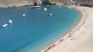 A coastal beach with clear blue waters, several boats, and a sandy shore with people and umbrellas. - Petra Traditional House (Andros)
