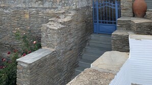 A stone building with a blue door and windows, featuring a stone staircase and a large pot. - Petra Traditional House (Andros)