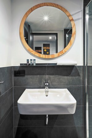 A modern bathroom with a rectangular sink, a wooden-framed mirror, and a dark tiled wall. - Stories by Grimm‘s (Münster)