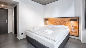 Una habitación de hotel moderna con una cama grande, un cabecero de madera, un estante empotrado con toallas y una puerta con pomo.