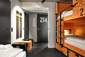 A modern hotel room with a bunk bed, a black door with the number 214, and a small wooden chest. - Stories by Grimm‘s (Münster)