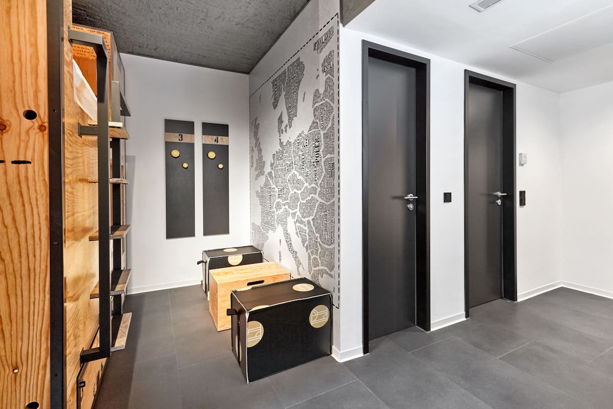 A modern hotel lobby with a minimalist design, featuring a wooden reception desk, a map wall, and two dark doors.