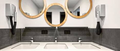 A modern bathroom with three sinks, two towel dispensers, and three wall-mounted mirrors.