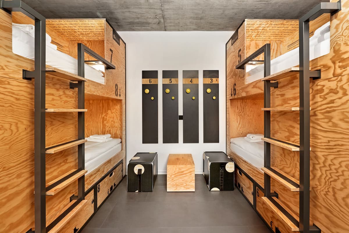 A bunk room with wooden bunk beds, a central table, and a wall with numbered lockers.