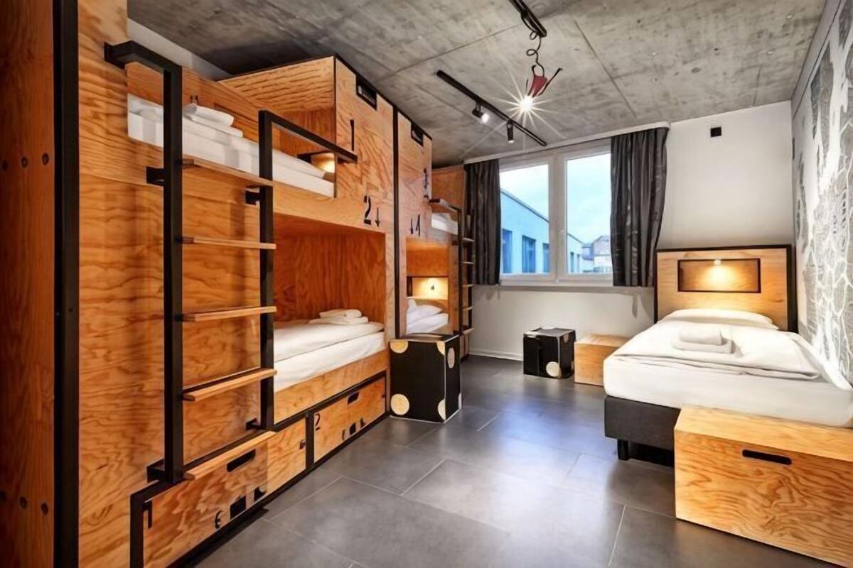 A room with bunk beds, a single bed, a window with curtains, and a hanging light fixture.