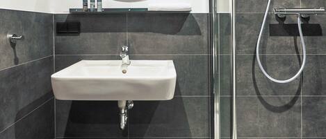 Un baño moderno con cabina de ducha de vidrio, un lavamanos blanco y un espejo con marco de madera.
