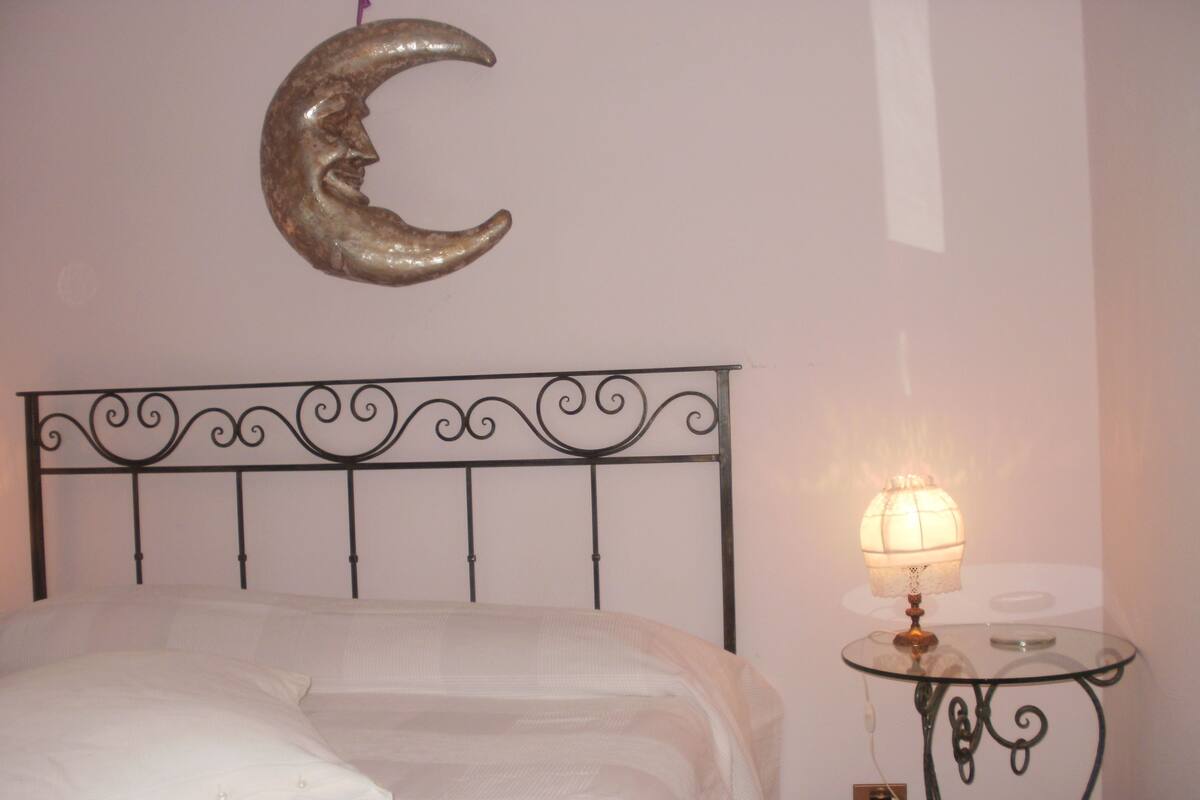Una cama con un almohadón blanco y una luna creciente decorativa en la pared.