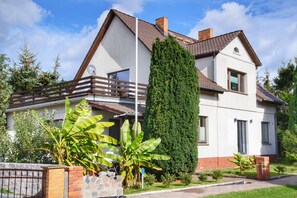 A two-story house with a balcony, a tall coniferous tree, and a brick wall.