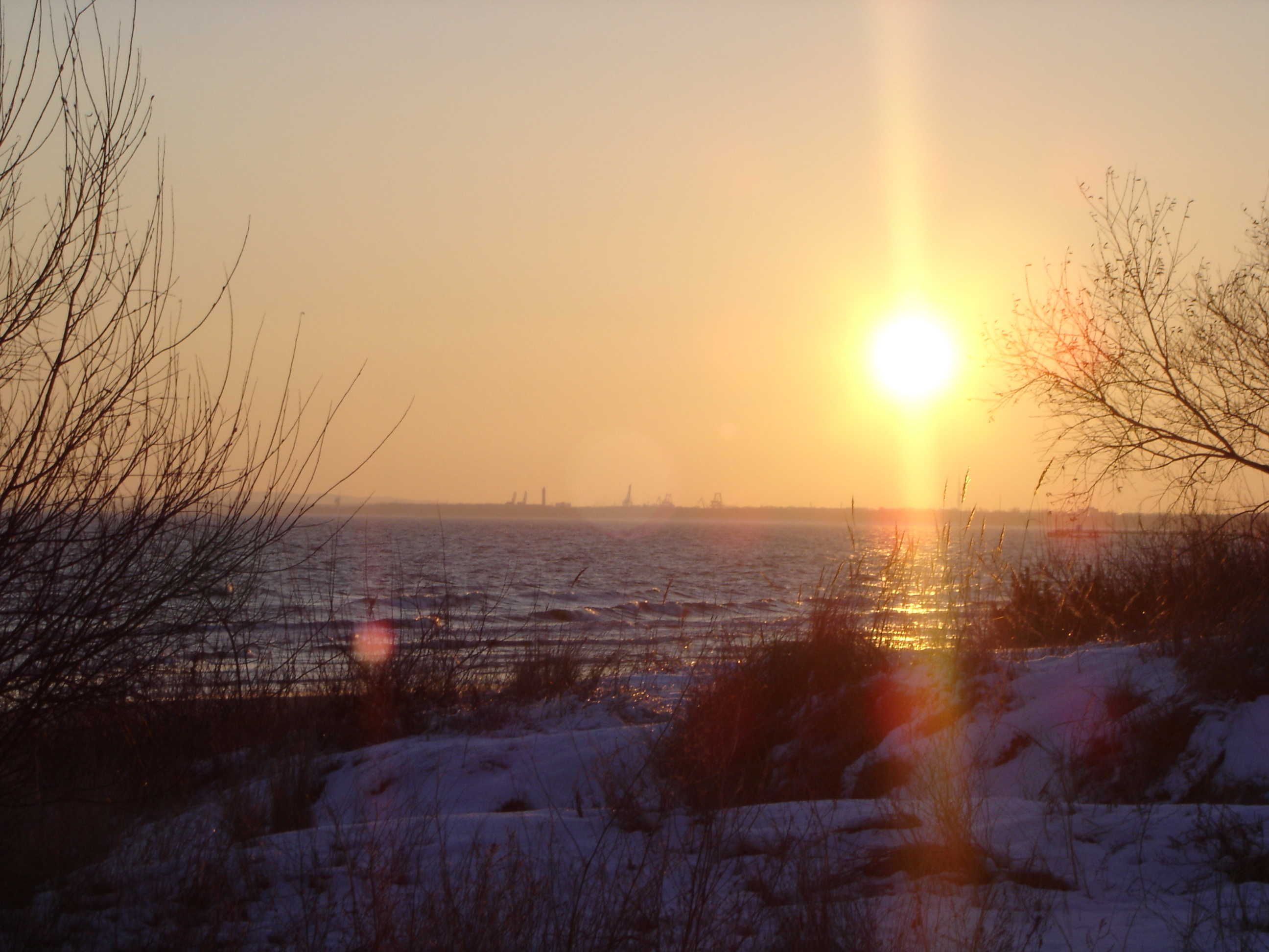A sunset over a frozen body of water with bare trees in the foreground.