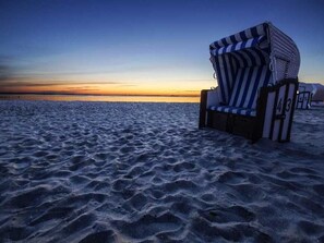 Une chaise de plage à rayures, une clôture en bois et une vue dégagée sur l’océan au coucher du soleil.