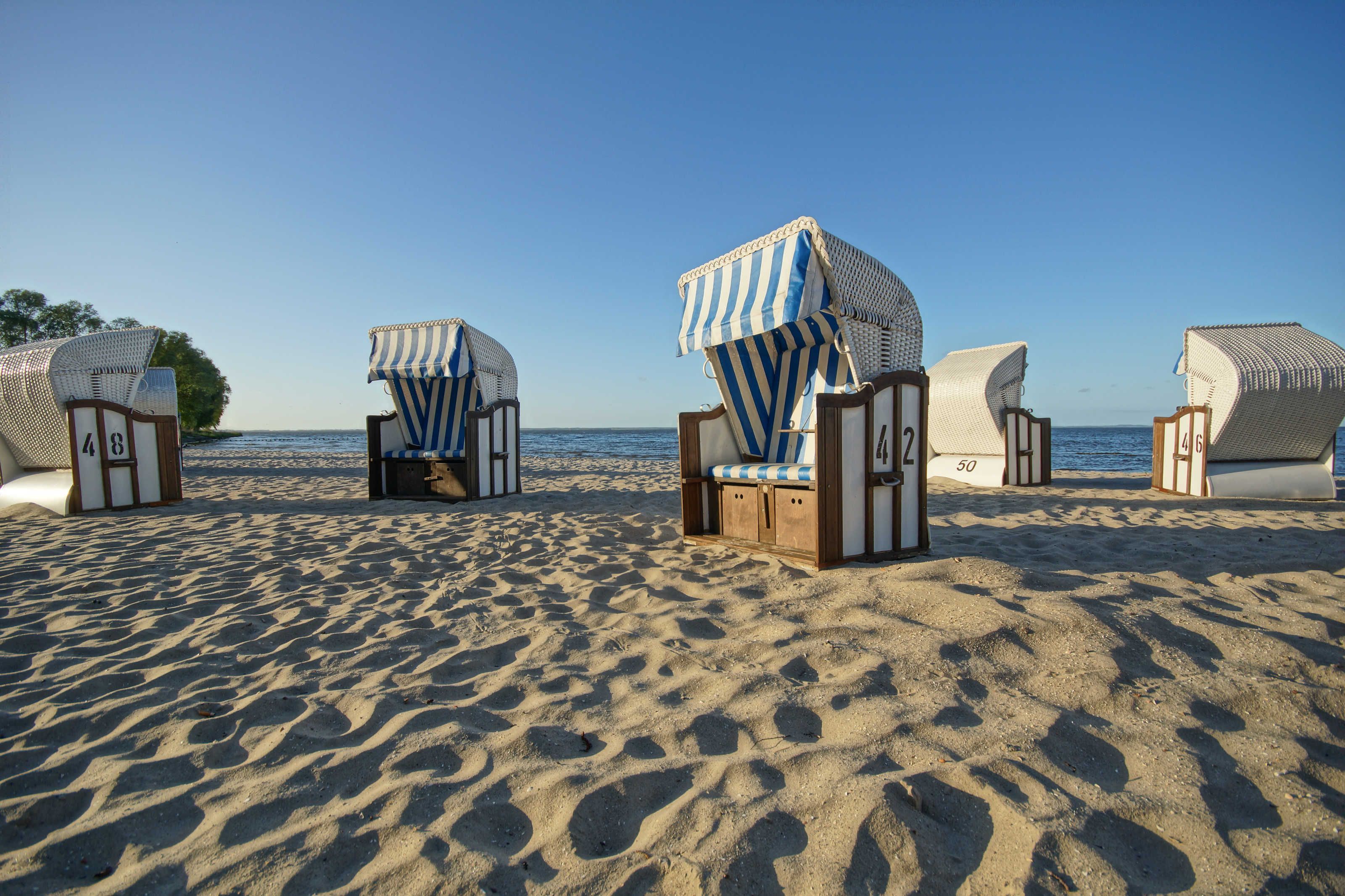 Strandstole med numre, en klar himmel og en sandstrand.