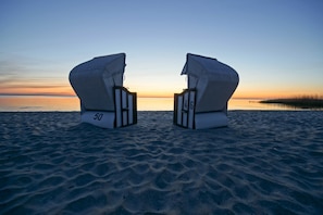 To strandstole med numrene 50 og 4G på ryglænet, placeret på en sandstrand med et roligt hav og en solnedgang i baggrunden.