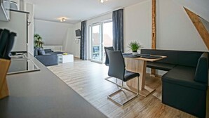Een modern appartement met keuken, eethoek en woonruimte, met een groot raam, een plant en een televisie.