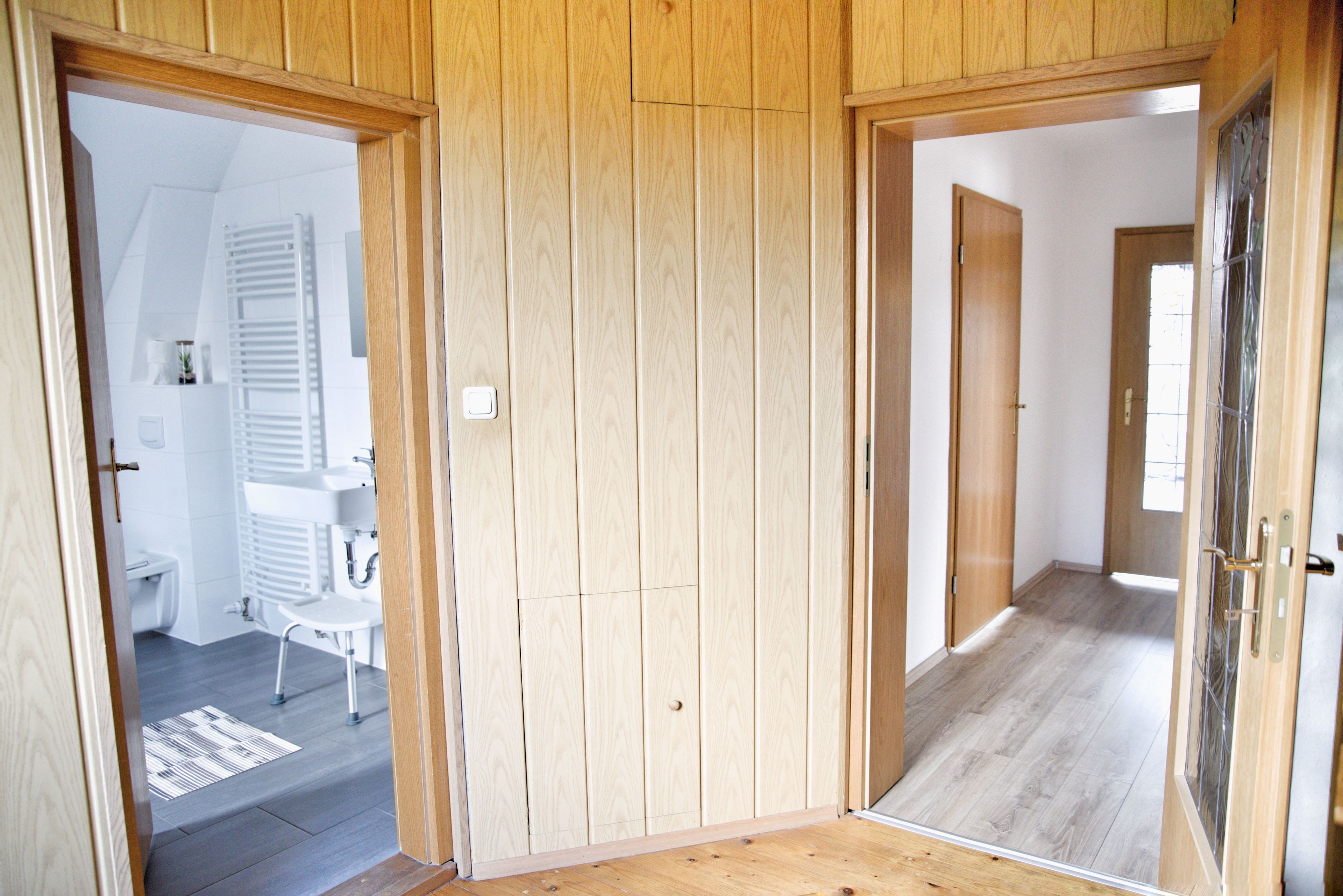 A hallway with wooden panel walls, a white radiator, and a white sink in a bathroom.