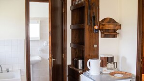 A compact kitchen with a refrigerator, coffee maker, and a shelf with kitchen utensils.