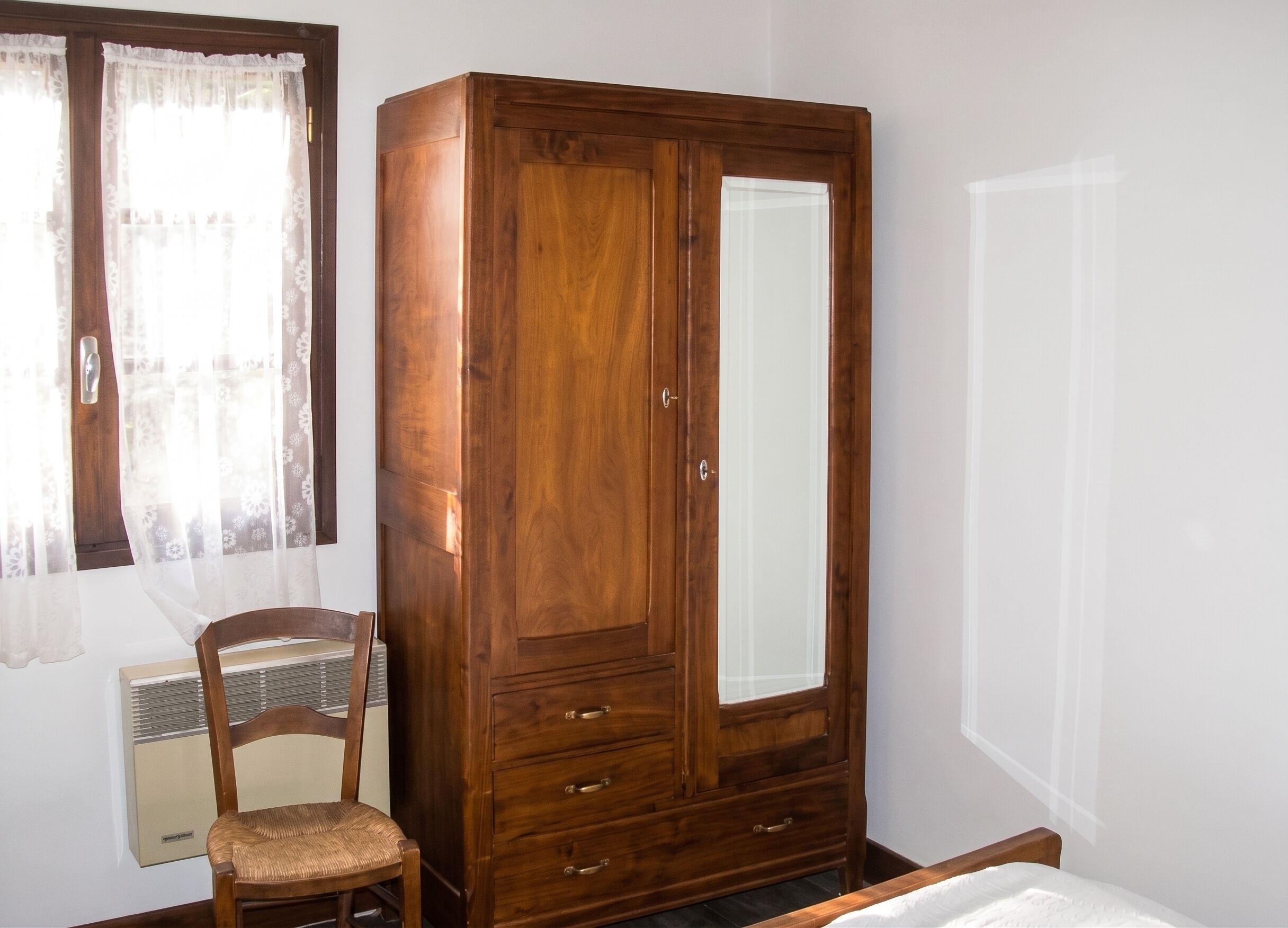 A wooden wardrobe with a mirror, a chair, and a radiator in a room with white walls.